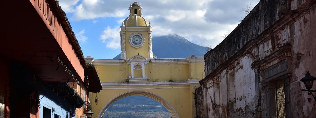 The iconic yellow Santa Catalina Arch in Antigua, a historic city famous for growing the Best Guatemalan Coffee Beans, with a volcano in the background.